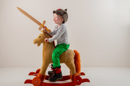 Funny child in old military cap with red star, on toy horse-rocking horse with wooden sword. Boy dreams of battles, victories and adventures. Concept training of spirit, education morale, patriotizm