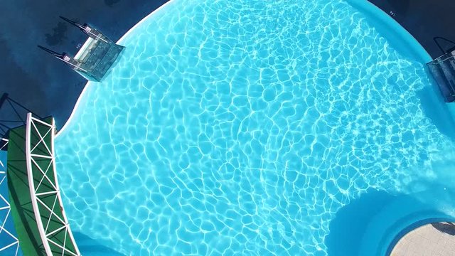 Top view of a condo swimming pool with two empty white deckchairs. Scene. Top view of luxury swimming pool. Exterior design. Empty poolside deckchairs with beautiful blue swimming pool