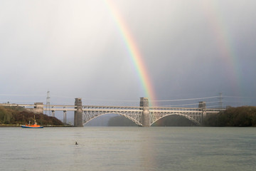 The Britannia Bridge, connecting Anglesey to mainland Wales in the UK, with a rainbow above it on a stormy winter day.