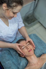 Top view of the face of a young girl during manual massage of the face in the spa. Shiatsu massage. Anti-aging facial massage for a beautiful blonde woman.
