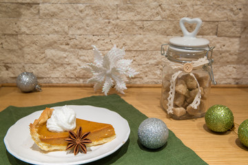 Traditional american pumpkin pie with whipped cream, whipped cream, cinnamon and almonds. Decorated with christmas green balls, brown sugar and snowflakes.