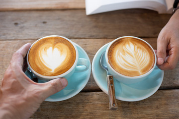 Hand Women and man put a Latte arts coffe hot coffee on wooden table.barista love art concept.