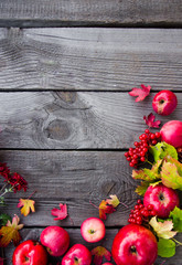 Many red apples lie on a wooden background, autumn colored, yellow leaves, viburnum, September, October, November, the background for the inscription, the frame for the signature
