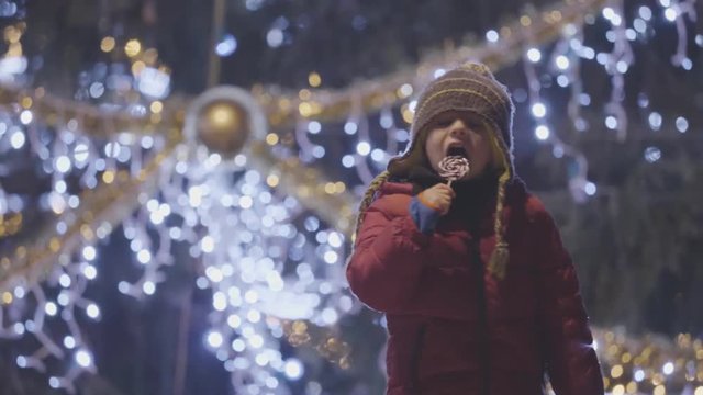 Funny child with lollipop at Christmas tree, outdoor night