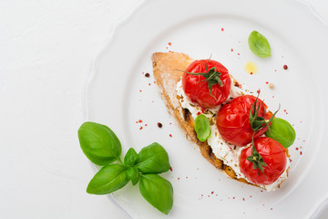 Sandwich with baked cherry tomatoes, garlic, olive oil and curd cheese on white background. Italian Cuisine. Top view.