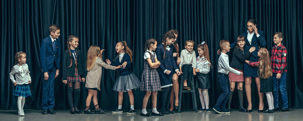 Cute smiling happy stylish children and female teacher on pink background. Beautiful stylish teen girls and boy standing together and posing on the school stage in front of the curtain. Classic style