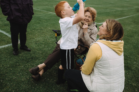 A young boy has a cold drink with his family during a half time break while playing sport