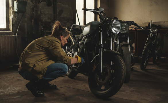 Young female working on restoration of old /vintage motorbikes in old rusty motorbike garage/workshop