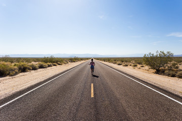 A young woman running down a long straight stretch of road in the desert