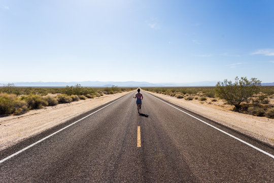 A Young Woman Running Down A Long Straight Stretch Of Road In The Desert