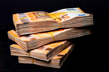 Pile of 50 real euro notes 50-euro banknotes under rubber band isolated on black. About 20000 euros...