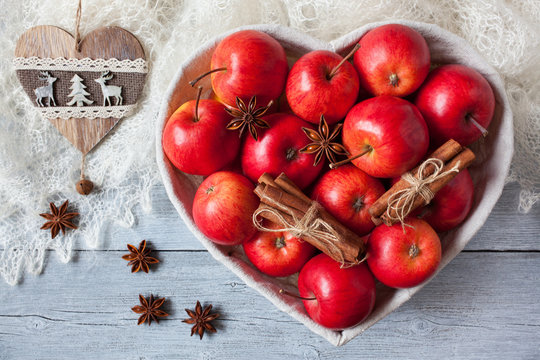 Red apples, cinnamon, anise in a basket in the shape of a heart on a table