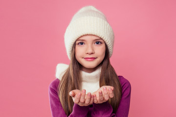 portrait cute little girl in warm knitted colored gray hat,scarf and mittens sending blowing a kiss air on pink background in studio.Children winter autumn clothes