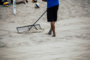The man prepares a beach volleyball court using the rake.