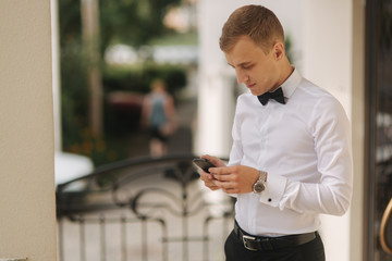 Obraz na płótnie Canvas Handsome man in shirt and bow tie use phone. blonde hair man outside