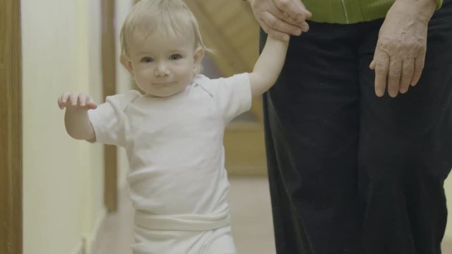 Grandmother holding baby on hand, toddler learning to walk indoor