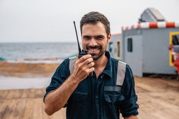 Marine Deck Officer or Chief mate on deck of vessel or ship . He holds VHF walkie-talkie radio in...