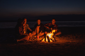 Camp on the beach. Group of young friends having picnic with bonfire. Man is playing guitar
