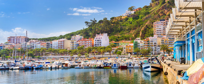 Fishing boats and yachts moored at pier in port Blanes. Motorboats with catch of sea fish, oysters, squid, sea delicacies. Fish auction for wholesalers and restaurants. Blanes, Spain, Costa Brava