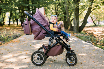Portrait of little cute toddler girl sitting in stroller or pram and going for a walk. Happy cute baby child having fun outdoors.