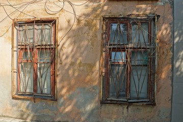 two old brown windows behind an iron grate on a concrete wall