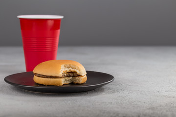 fast food with delicious bitten hamburger on the background of a red Cup with a drink.