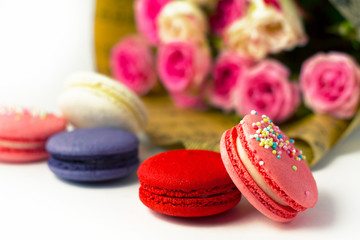  Multi-colored macaroons on the background of a bouquet of pink flowers.