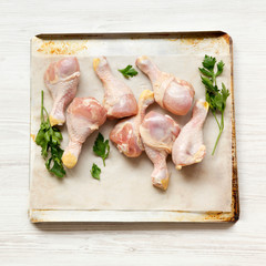 Uncooked raw chicken legs on a baking sheet paper on tray over white wooden background, top view. Close-up.