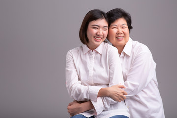 Beautiful senior mom and her adult daughter are hugging, looking at camera and smiling