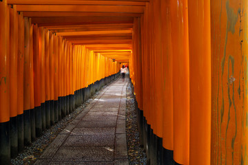 In the distance a woman walks through the Fushimi Inari Taisha Torii shrines in Kyoto, Japan, showing motion blur