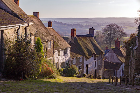 Famous view of Gold Hill in Shaftesbury village, Dorset, England, UK, with beautiful countryside in the background