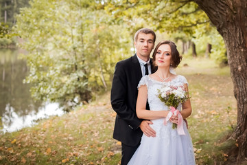 Wedding couple. Bride and groom are embracing in the yellow autumn park against the background of a river. Newlyweds