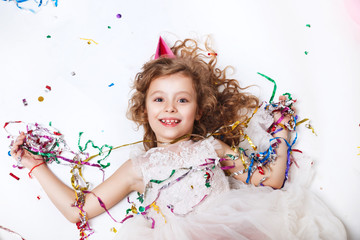 Holidays concept. Little funny girl lying in multicolored confetti on birthday party