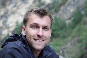 A handsome young Caucasian rugged man dressed warmly for outdoor activities such as hiking, outdoors, smiles happy at the camera, with room for text / copy.