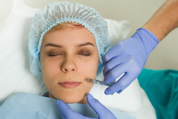 Top view of lips augmentation procedure on a young woman done by a cosmetologist doctor with...