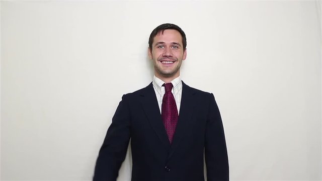 Young handsome businessman in blue suit, greeting partners waving one and two hands.Portrait on a white background.