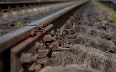 Selective field of focus. Detail of rusty screws and nut on old railroad track. Concrete tie with rusty nuts and bolts. Damaged surface of rail rod. No train passed this railroad for a long time
