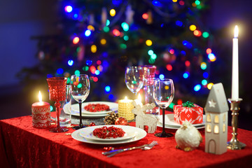 Beautiful table setting for Christmas party or New Year celebration at home. Cozy room with a fireplace and Christmas tree in a background.