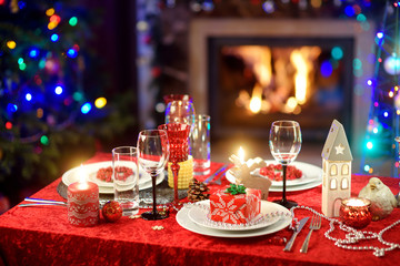 Beautiful table setting for Christmas party or New Year celebration at home. Cozy room with a fireplace and Christmas tree in a background.