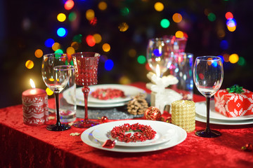 Beautiful table setting for Christmas party or New Year celebration at home. Cozy room with a fireplace and Christmas tree in a background.