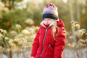 Adorable little girl having fun in beautiful winter park. Cute child playing in a snow. © MNStudio