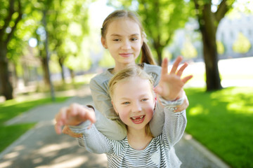Two adorable sisters laughing and hugging on warm and sunny summer day in a park