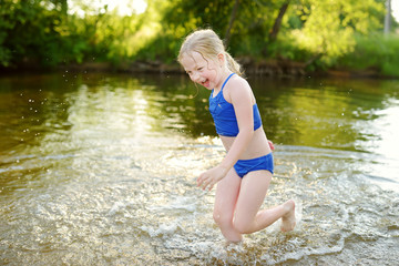 Cute little girl wearing swimsuit playing by a river on hot summer day. Adorable child having fun outdoors during summer vacations.