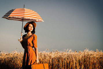 portrait of the beautiful young woman with red umbrella and brown suitcase standing on the field