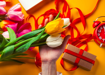 Female hands are holding a tulip flower before wrapping on yellow background