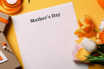 Beautiful bouquet of tulips and paper with words Mothers day and gifts around on yellow background