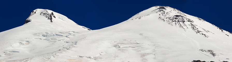 Obraz premium Panoramic view of the southern slope of Mount Elbrus of the Caucasus Mountains in Russia. Snow-covered mountain peaks with two peaks.