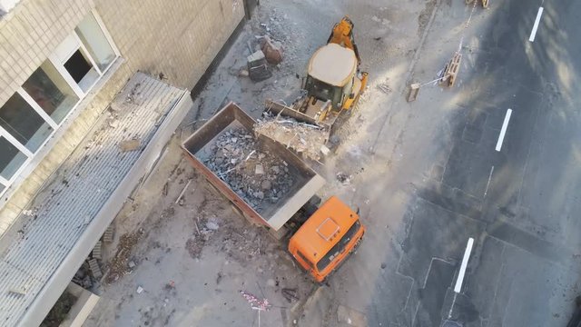 Bulldozer loader uploading waste and debris into dump truck at construction site. building dismantling and construction waste disposal service. Aerial drone industrial background