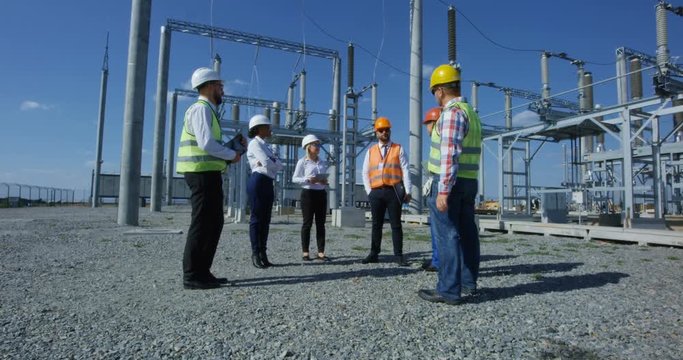 Group of adult diverse men in hardhats gathering on transformer platform of solar electrical plant having discussion
