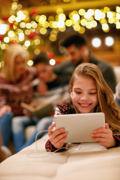 little girl with headphones is using a tablet on Christmas day.